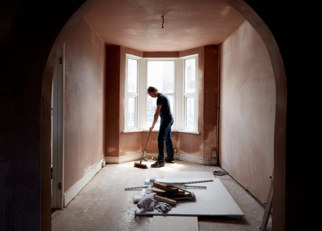 A builder sweeping and tidying up in a renovated replastered house with an archway.